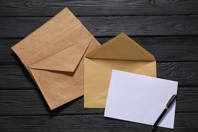 Kraft paper envelopes with letter and pen on black wooden background, flat lay. Mockup for design