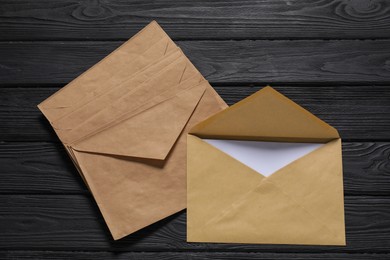 Photo of Kraft paper envelopes with letter on black wooden background, top view. Mockup for design