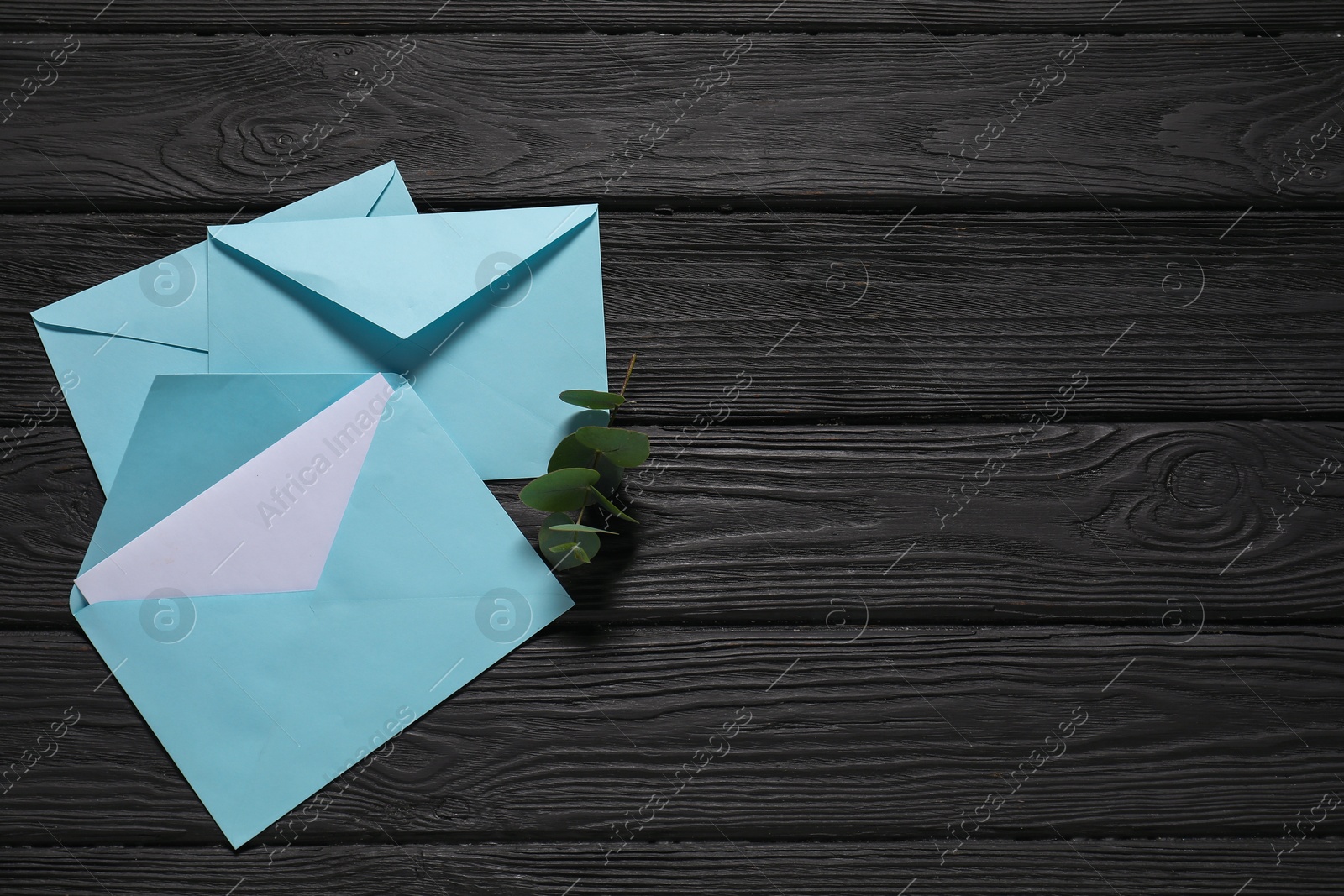 Photo of Paper envelopes with letter and eucalyptus branch on black wooden background, flat lay. Mockup for design