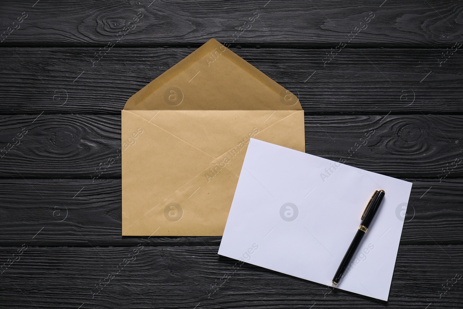 Photo of Kraft paper envelope with letter and pen on black wooden background, flat lay. Mockup for design