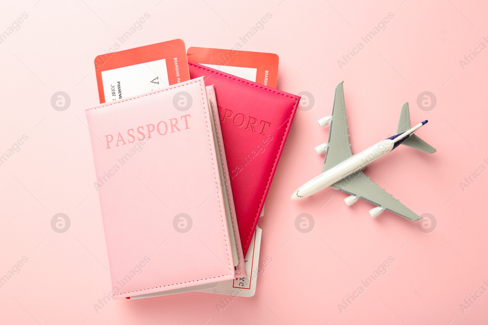 Photo of Passports with tickets and plane model on pink background, flat lay