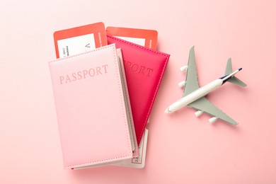 Photo of Passports with tickets and plane model on pink background, flat lay