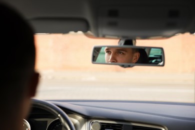 Photo of Driver behind steering wheel of modern car, view through rear mirror