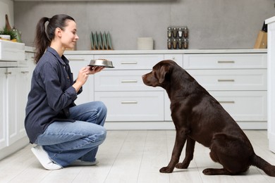 Photo of Woman giving bowl with dry pet food to her dog indoors