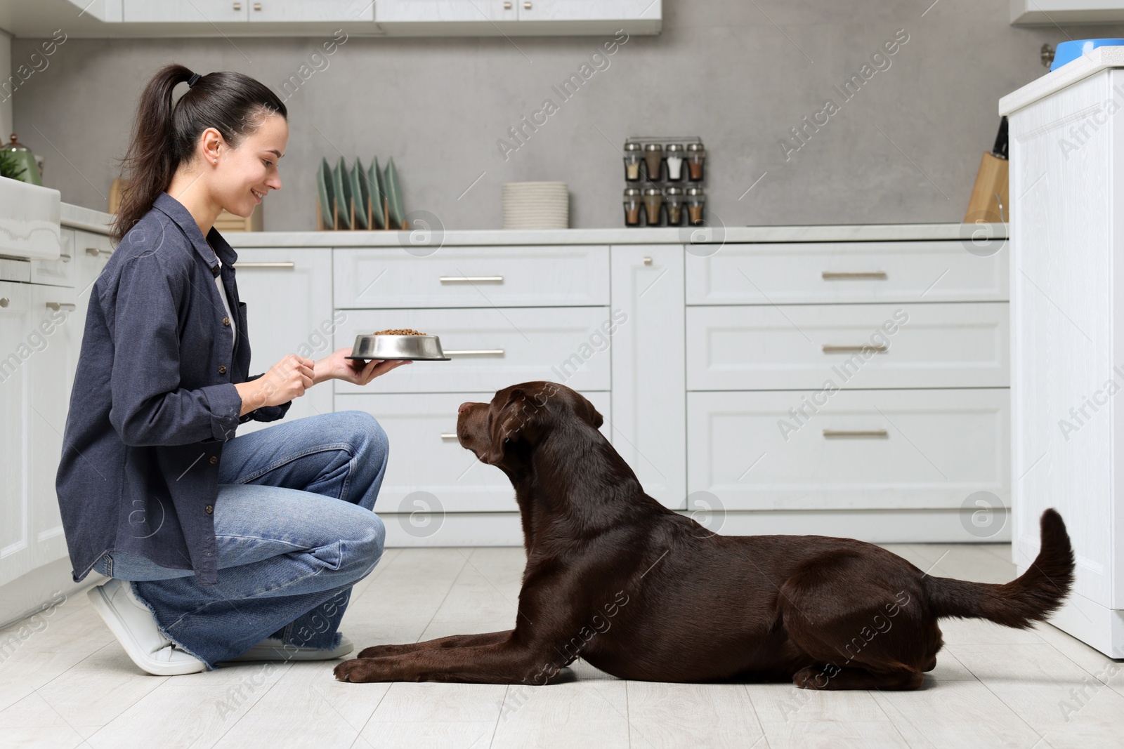 Photo of Woman giving bowl with dry pet food to her dog indoors