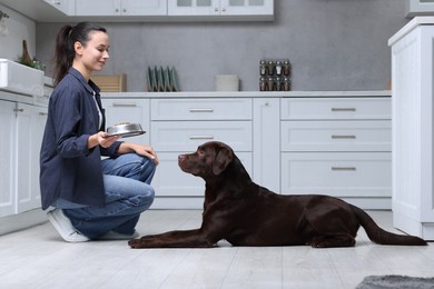 Photo of Woman giving bowl with dry pet food to her dog indoors