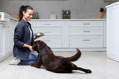 Photo of Woman with feeding bowl giving dry pet food to her dog indoors