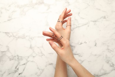 Photo of Woman wearing beautiful rings at white marble table, top view