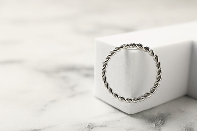 Photo of Stylish presentation of ring on white marble table, closeup. Space for text