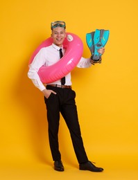 Photo of Businessman with inflatable ring, flippers and diving mask on orange background