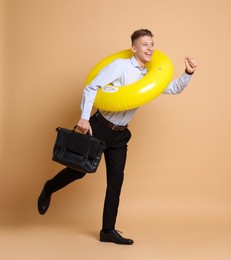 Photo of Businessman with inflatable ring and briefcase on beige background