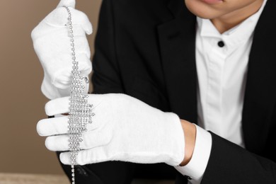 Photo of Appraiser in gloves with luxury necklace on beige background, closeup