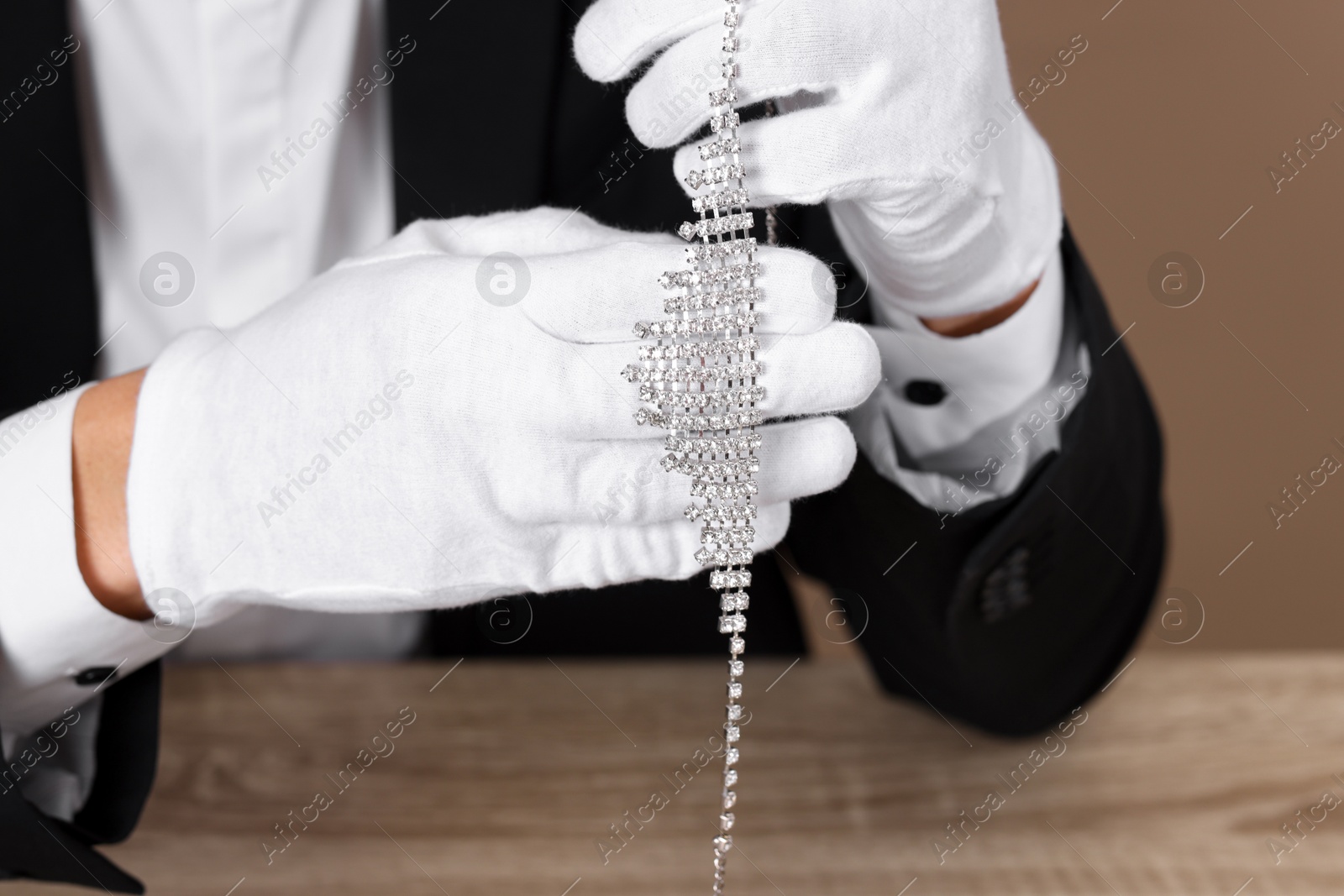 Photo of Appraiser in gloves with luxury necklace at wooden table, closeup