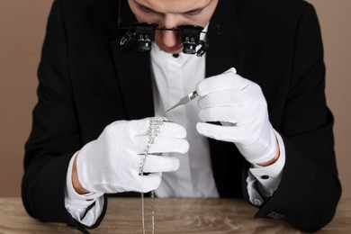 Photo of Appraiser with tweezers evaluating luxury necklace at wooden table