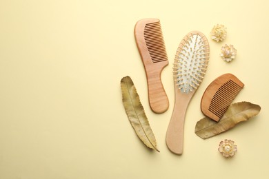 Photo of Wooden hair brush, combs, flowers and leaves on beige background, flat lay. Space for text