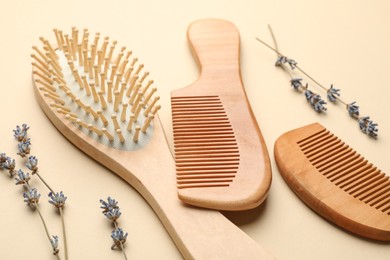 Photo of Wooden hair brush, combs and lavender flowers on beige background, closeup