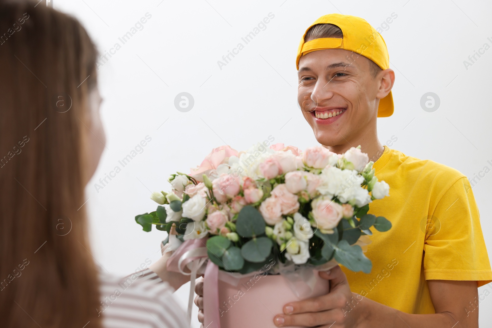 Photo of Happy delivery man giving gift box with beautiful floral composition to woman at door