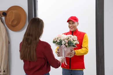 Photo of Happy delivery man giving gift box with beautiful floral composition to woman at door