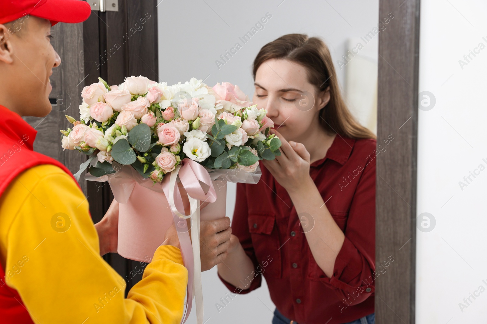 Photo of Woman smelling beautiful flowers from delivery man at door