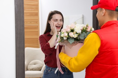 Photo of Delivery man giving gift box with beautiful floral composition to surprised woman at door