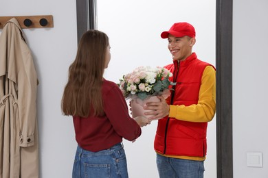 Photo of Smiling delivery man giving gift box with beautiful floral composition to woman at door