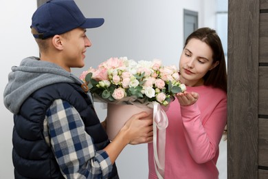 Photo of Woman receiving gift box with beautiful floral composition from delivery man at door