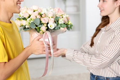 Photo of Happy delivery man giving gift box with beautiful floral composition to woman indoors, closeup