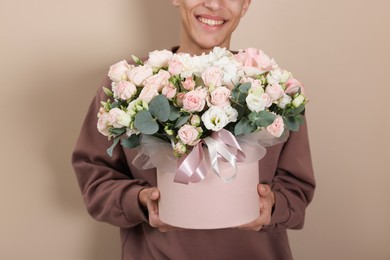 Photo of Smiling delivery man holding gift box with beautiful floral composition on beige background, closeup