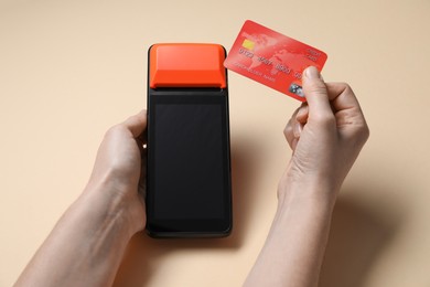 Photo of Woman with credit card using payment terminal on beige background, closeup