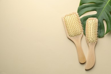 Photo of Wooden hair brushes and monstera leaf on beige background, flat lay. Space for text