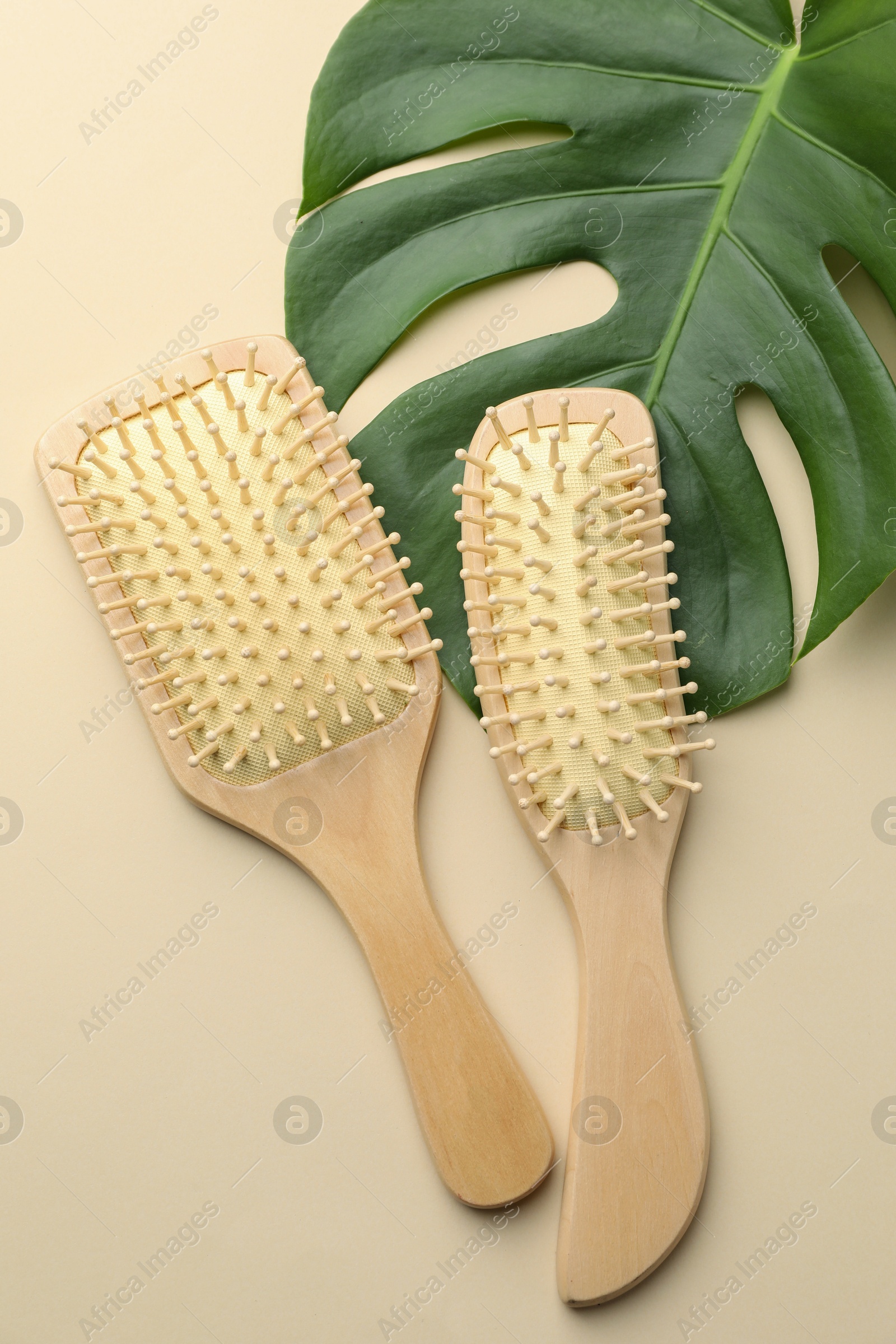 Photo of Wooden hair brushes and monstera leaf on beige background, flat lay