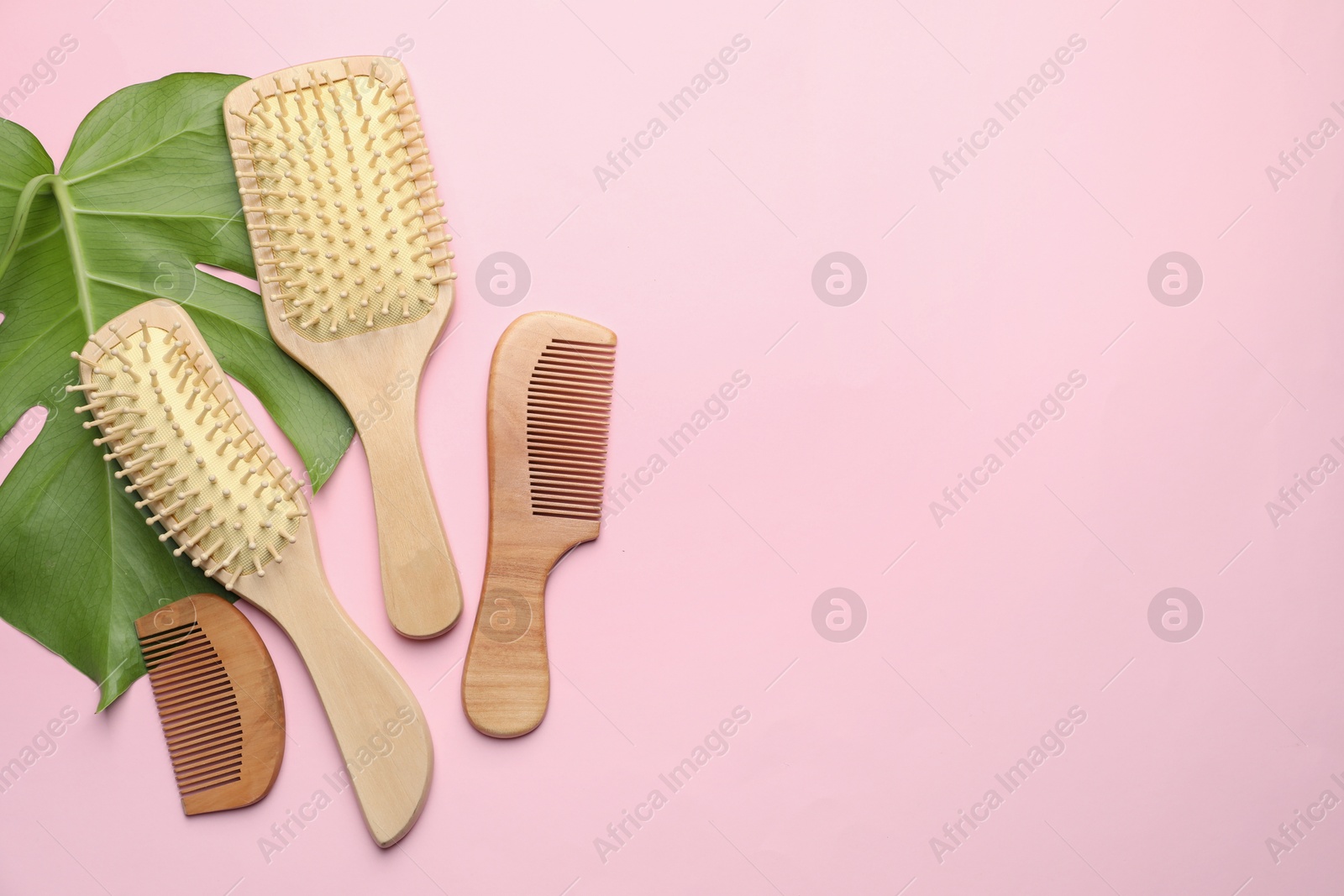 Photo of Wooden hair brushes, combs and monstera leaf on pink background, flat lay. Space for text