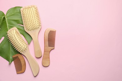 Photo of Wooden hair brushes, combs and monstera leaf on pink background, flat lay. Space for text