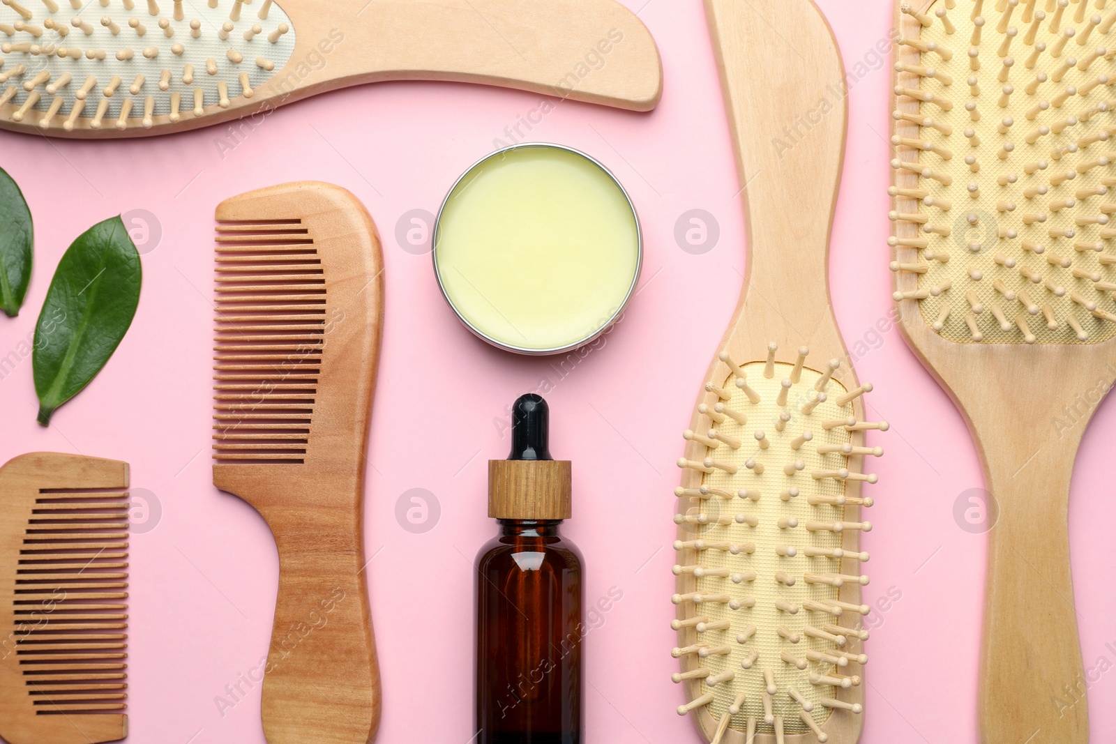 Photo of Wooden hair brushes, combs, cosmetic products and green leaves on pink background, flat lay