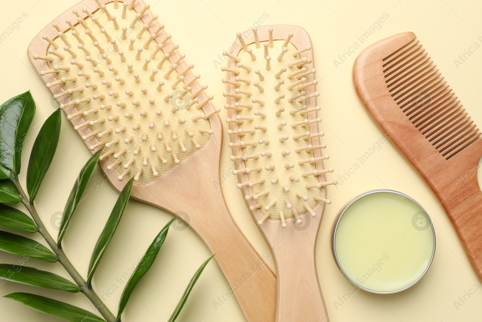 Photo of Wooden hair brushes, comb, wax and green branch on beige background, flat lay