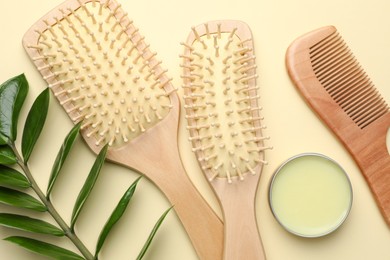 Photo of Wooden hair brushes, comb, wax and green branch on beige background, flat lay