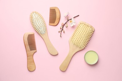 Photo of Wooden hair brushes, combs, wax and orchid branch on pink background, flat lay