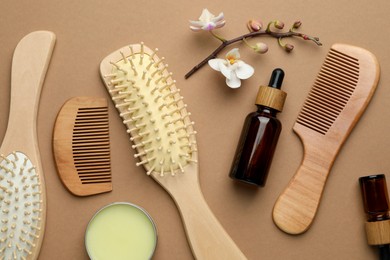 Photo of Wooden hair brushes, combs, cosmetic products and orchid branch on dark beige background, flat lay