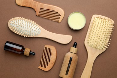 Photo of Wooden hair brushes, combs and cosmetic products on dark beige background, flat lay