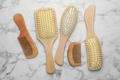 Photo of Wooden hair brushes and combs on white marble table, flat lay