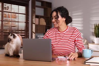 Photo of Beautiful woman with her cute cat working on laptop at desk in home office