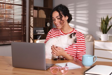 Photo of Beautiful woman with her cute cat working on laptop at desk in home office