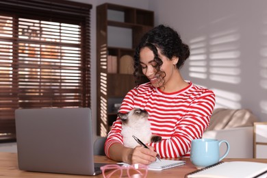 Photo of Beautiful woman with her cute cat working on laptop at desk in home office