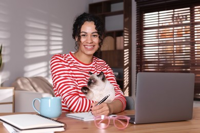 Photo of Beautiful woman with her cute cat working on laptop at desk in home office