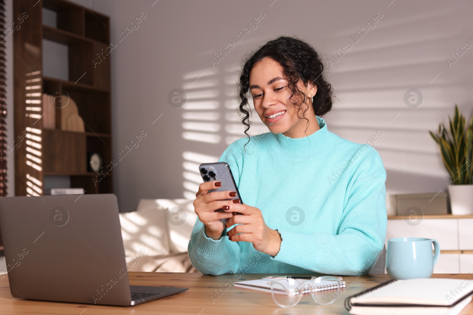 Photo of Beautiful woman working with smartphone and laptop at desk in home office