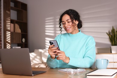 Photo of Beautiful woman working with smartphone and laptop at desk in home office