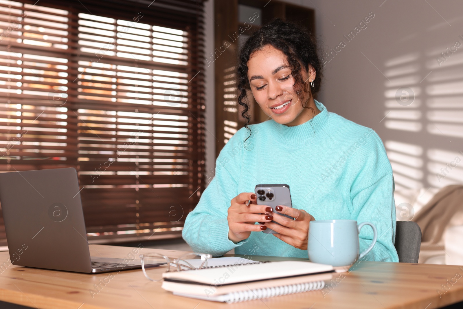 Photo of Beautiful woman working with smartphone and laptop at desk in home office