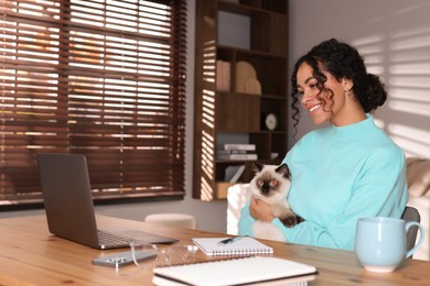 Photo of Beautiful woman with her cute cat working on laptop at desk in home office