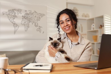 Photo of Beautiful woman with her cute cat working on laptop at desk in home office