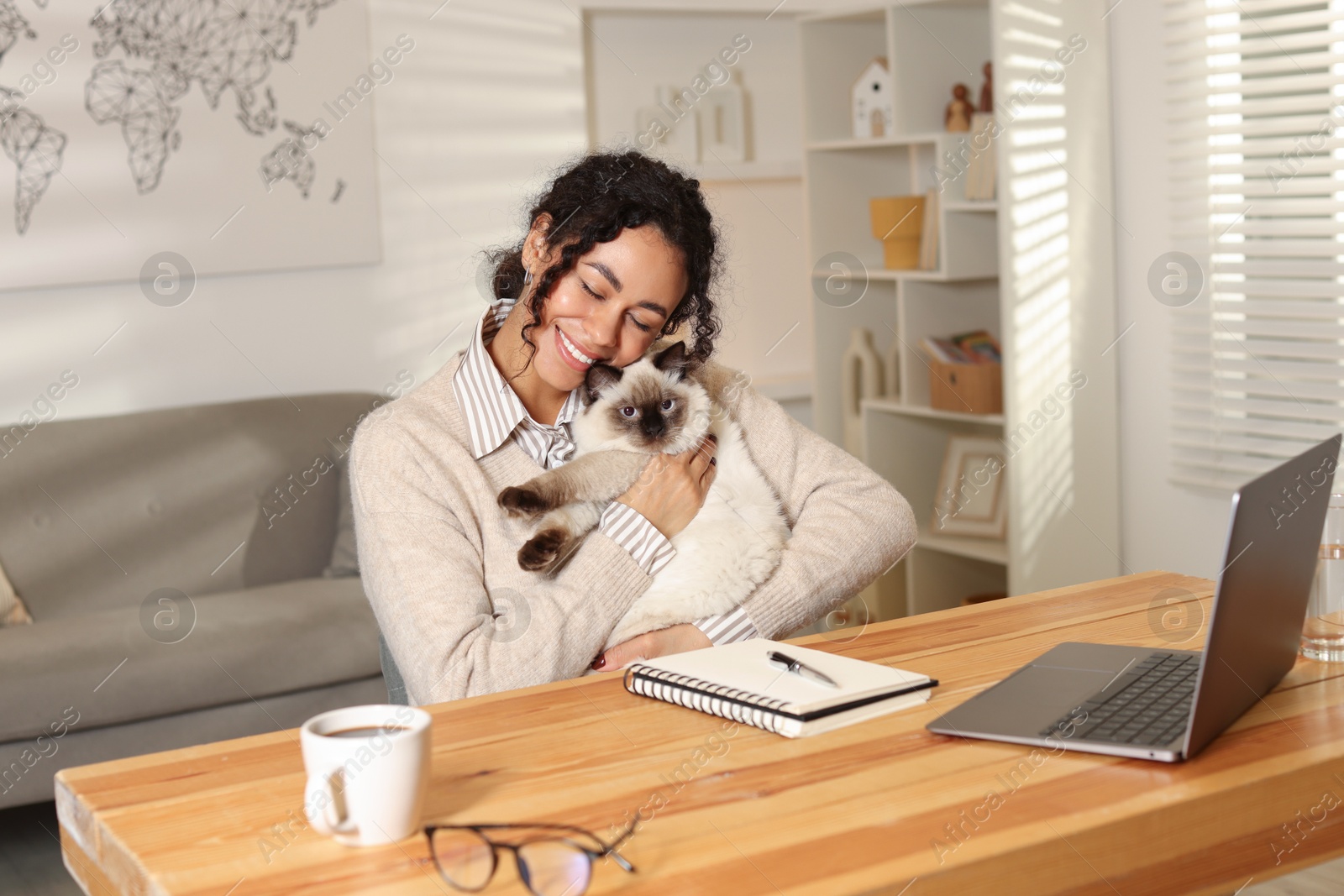 Photo of Beautiful woman with her cute cat working on laptop at desk in home office